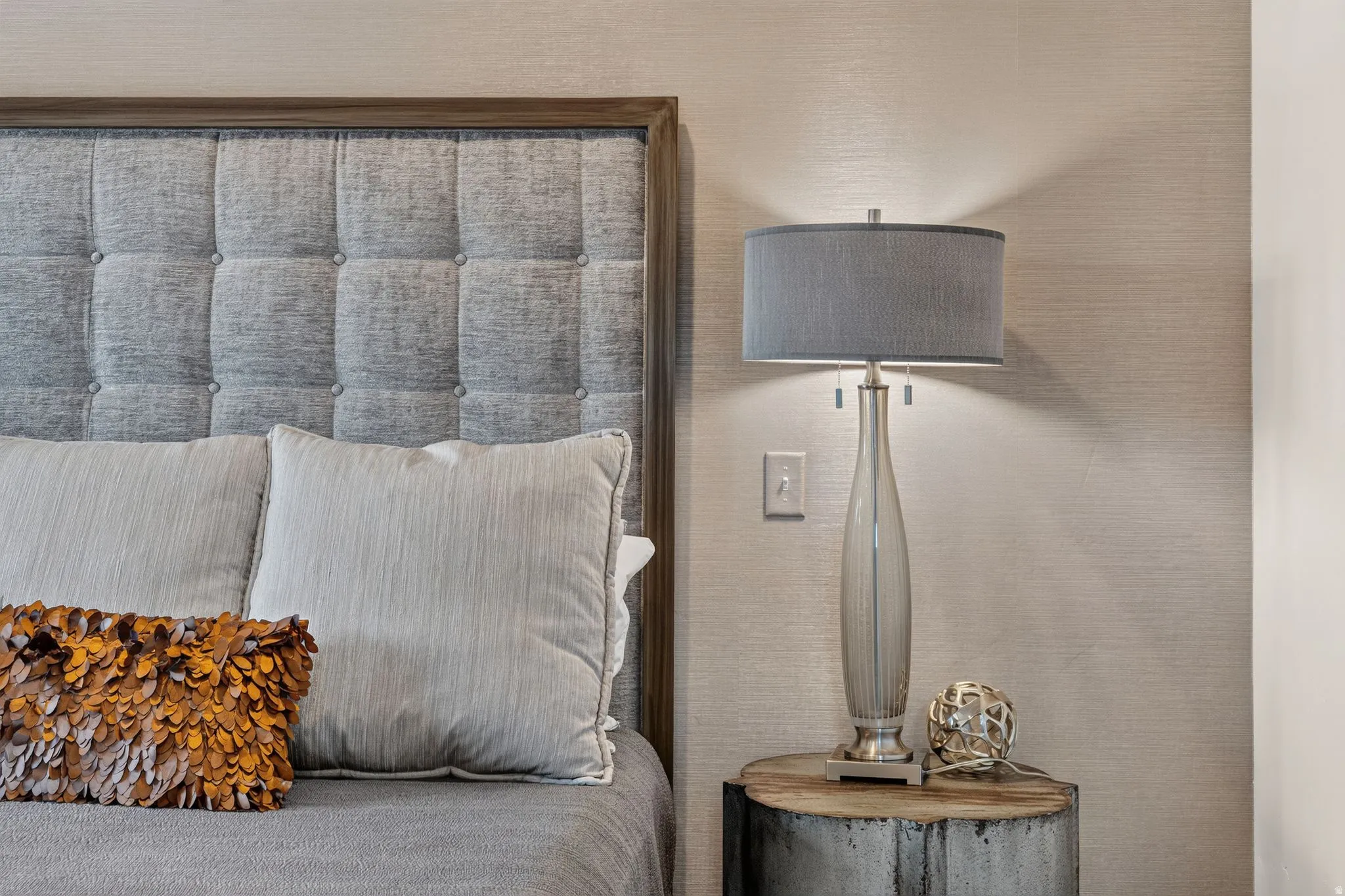Tufted fabric headboard with a wood-finish frame, textured wall covering, and a bedside table with a natural wood top