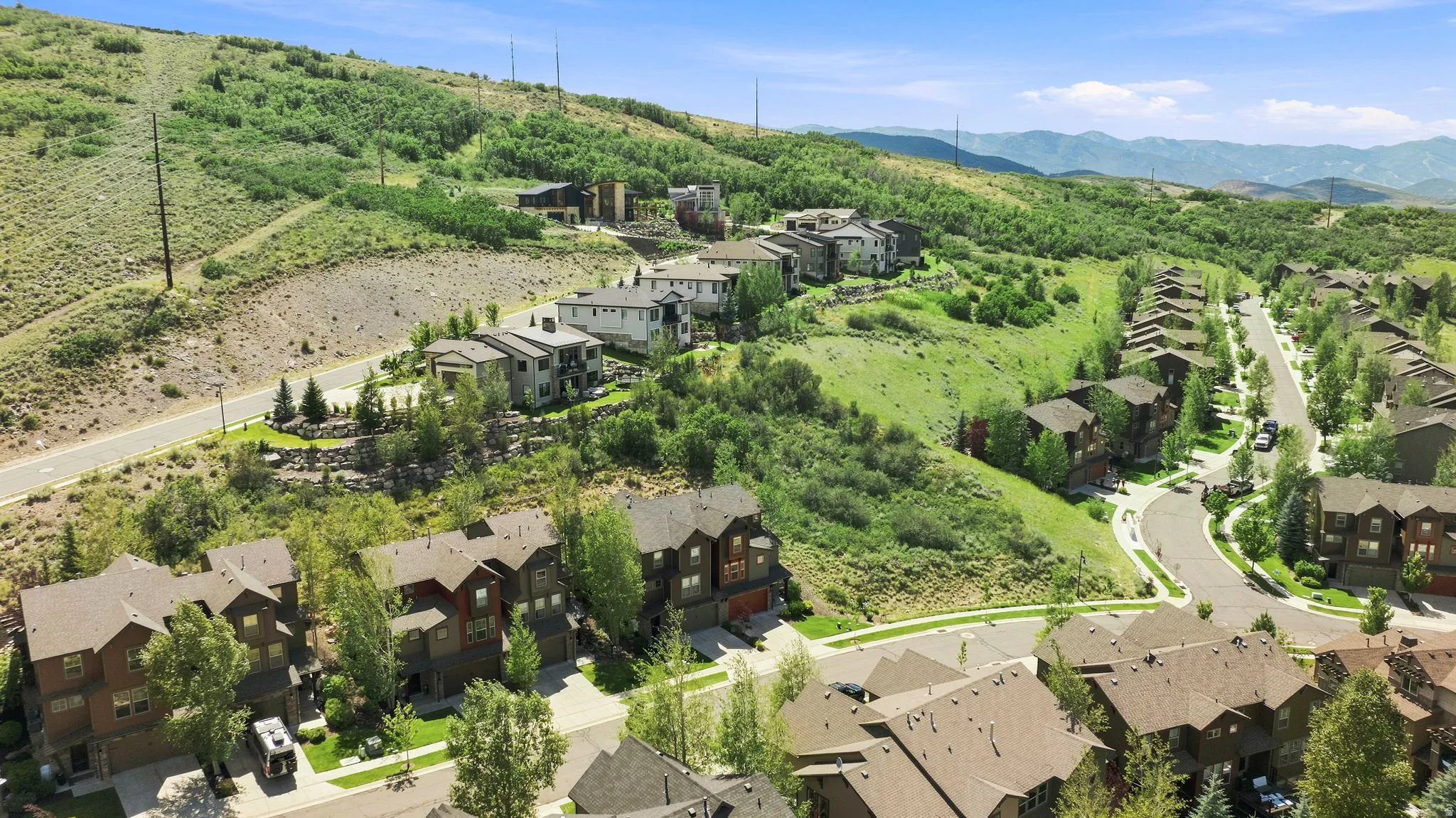 Aerial perspective showcasing a residential community nestled on a verdant hillside with paved streets and mature trees