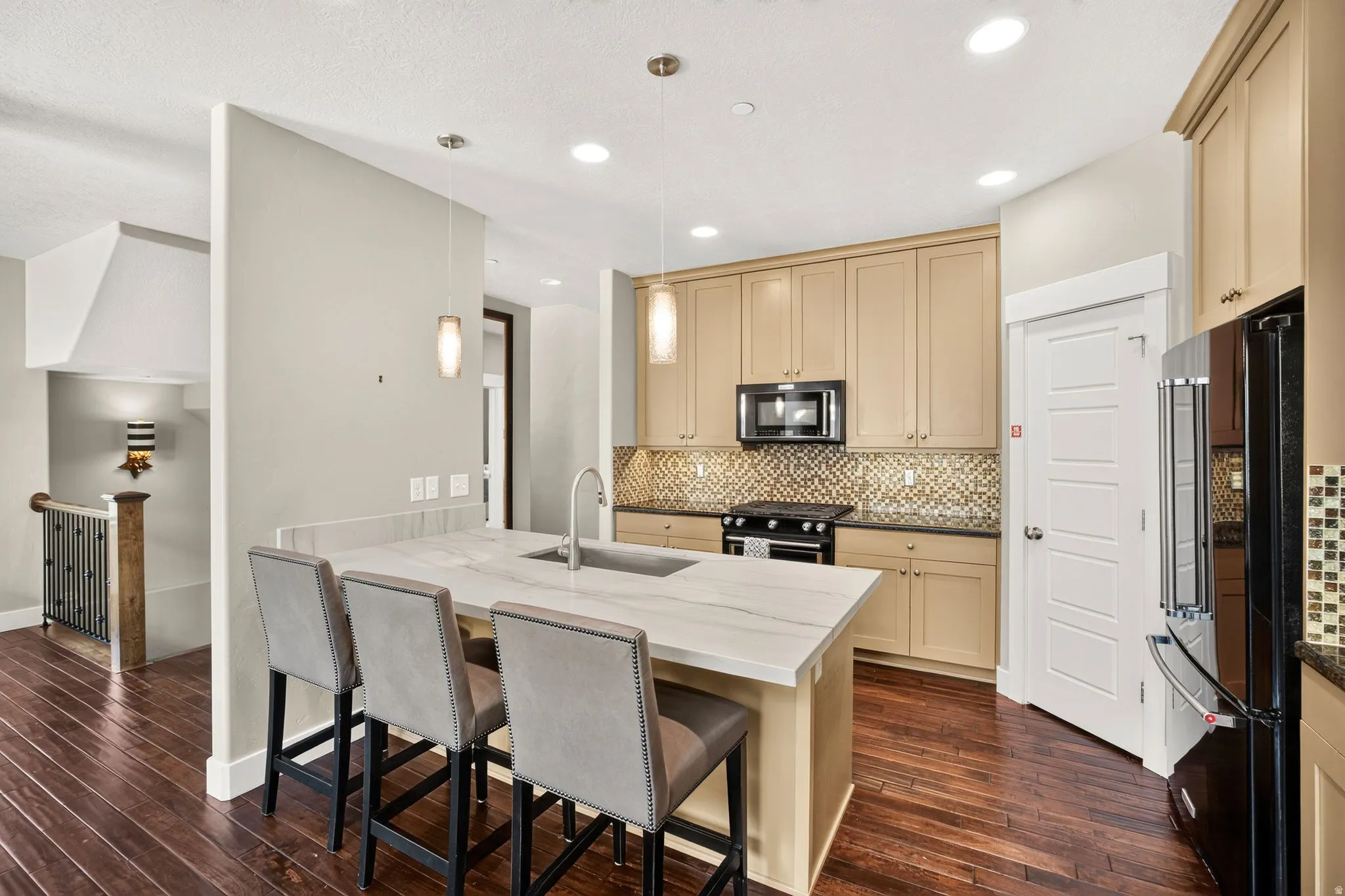 Gourmet kitchen featuring a large island with seating, pendant lighting, stainless steel sink, wood-finish flooring, and a tiled backsplash