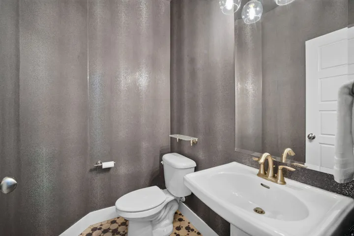 Powder room featuring a pedestal sink, brass-finish faucet, and an overhead vanity light fixture