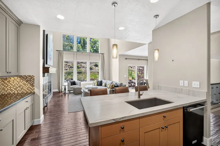Open-concept living area featuring a kitchen island with an undermount sink and pendant lighting, wood-finish flooring, a contemporary fireplace, and large windows providing natural light