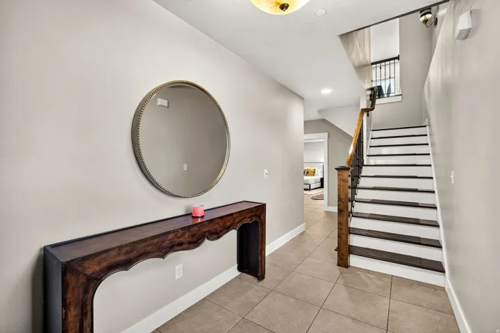 Tiled entryway featuring a staircase with painted risers and dark wood-finish treads, a wood newel post, and wrought iron balusters
