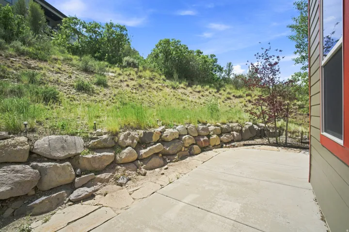 Concrete patio area featuring a natural stone retaining wall and hillside landscaping