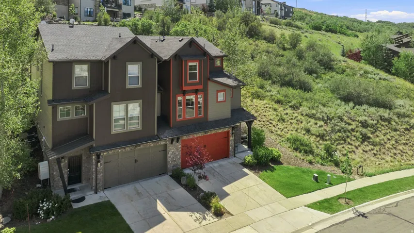 Contemporary multi-story residence featuring a dark brown and red exterior, two attached garages with red doors, and a paved driveway