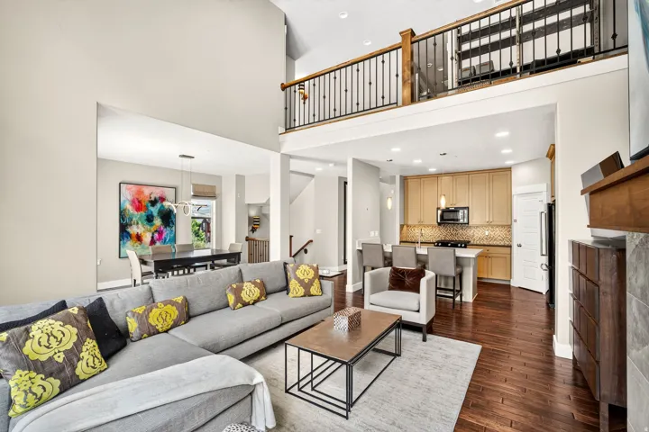 Open-concept living area featuring high ceilings, wood-finish flooring, a kitchen with light-tone cabinetry and stainless steel appliances, a breakfast bar, and an open loft overlooking the space