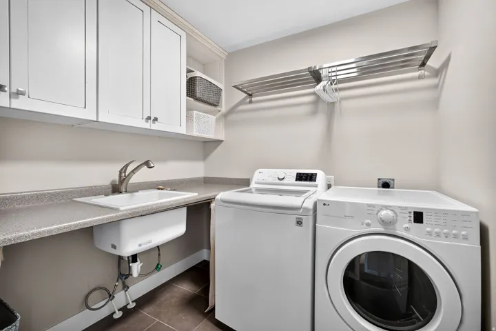 Laundry area featuring white cabinetry, a built-in utility sink, a spacious countertop, and a wall-mounted drying rack