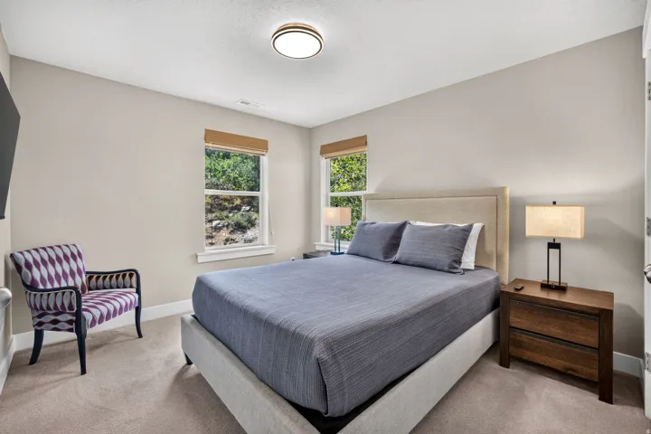 Bedroom featuring plush carpet flooring, neutral paint palette, two windows with natural wood blinds, and a flush mount ceiling light fixture