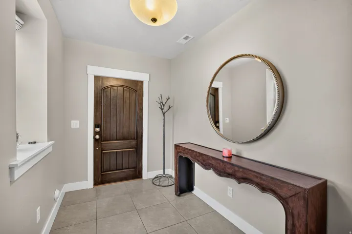Entryway featuring a paneled wood door with white trim, a decorative round mirror, and tile flooring