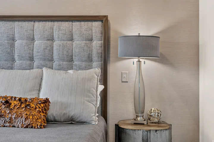 Tufted fabric headboard with a wood-finish frame, textured wall covering, and a bedside table with a natural wood top