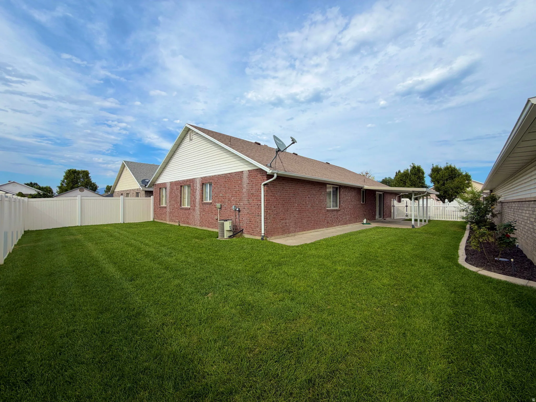 Expansive backyard featuring a lush lawn, privacy fencing, brick exterior, and a covered patio area
