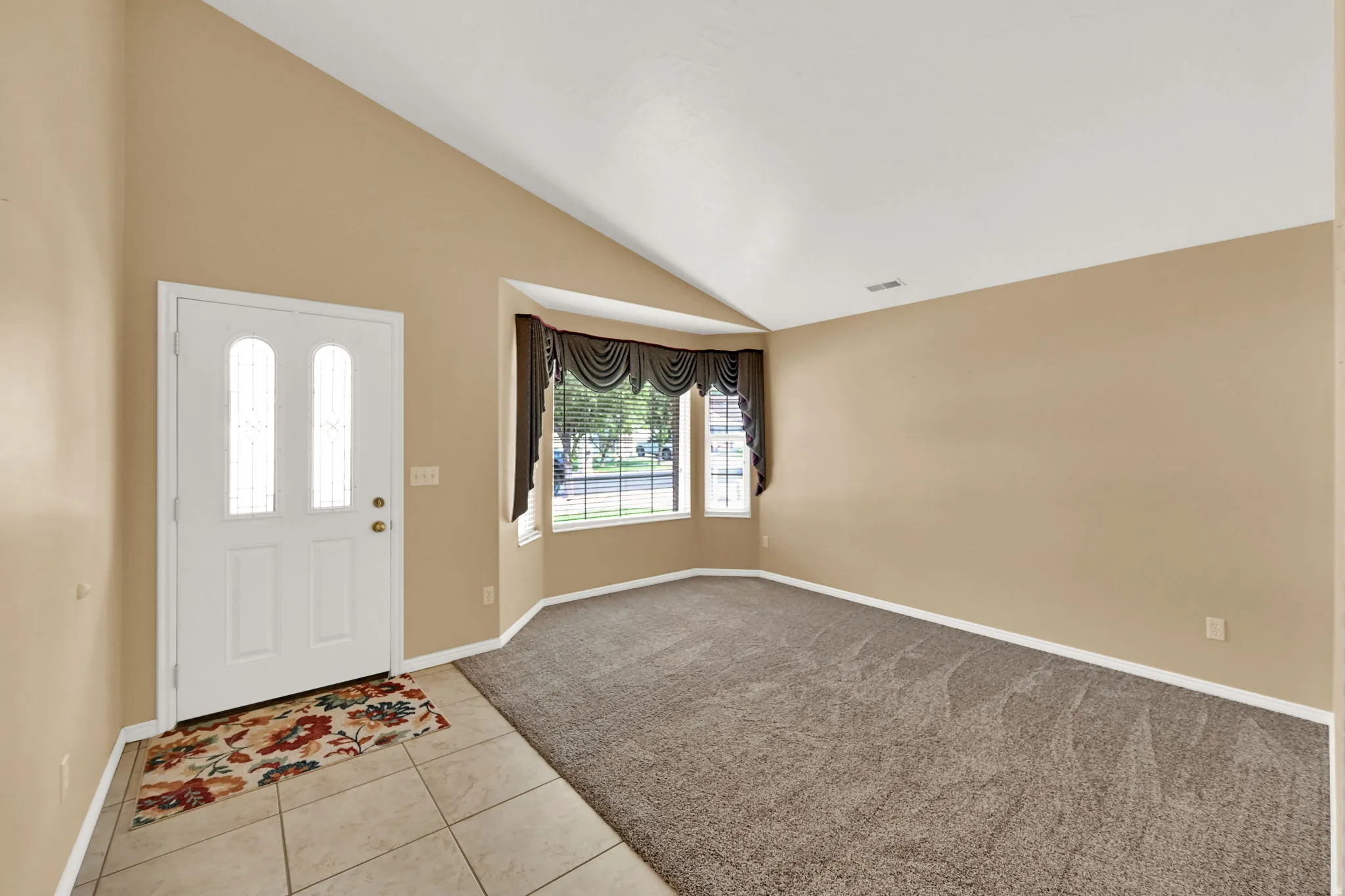 Entryway featuring a white door with decorative glass panels, leading to a living space with vaulted ceilings and a bay window
