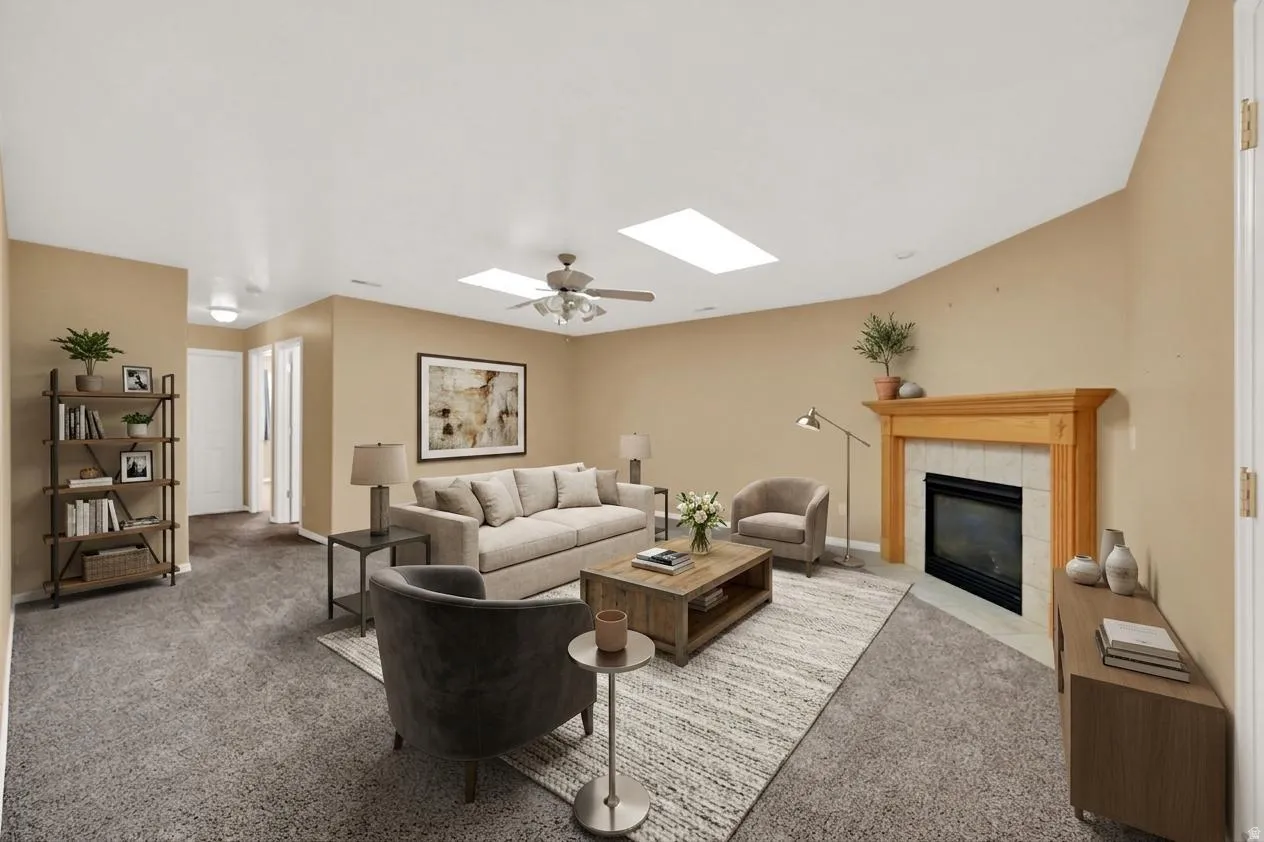 Virtually staged spacious family  room area featuring a fireplace with a wood mantel, overhead skylights, and a ceiling fan
