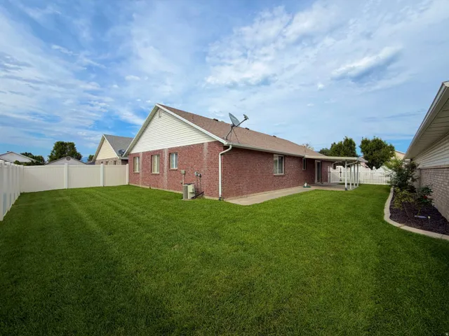 Expansive backyard featuring a lush lawn, privacy fencing, brick exterior, and a covered patio area