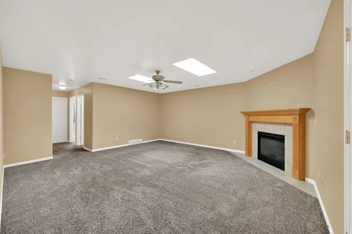 Spacious room featuring a fireplace with a wood mantle and tiled surround, two skylights, and a ceiling fan