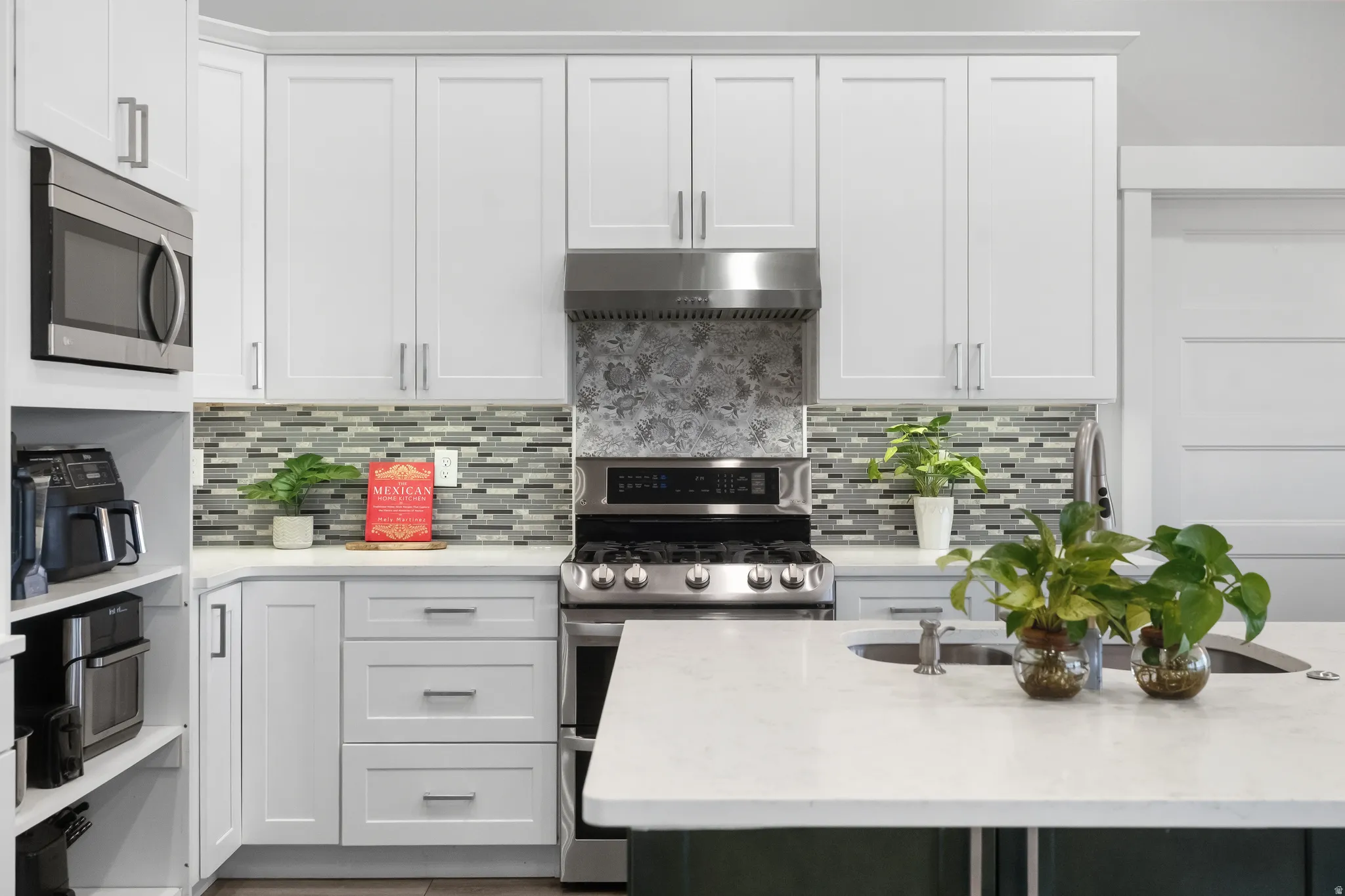 Modern kitchen featuring white shaker-style cabinetry, a built-in stainless steel microwave, a gas range with a matching range hood, and a mosaic tile backsplash