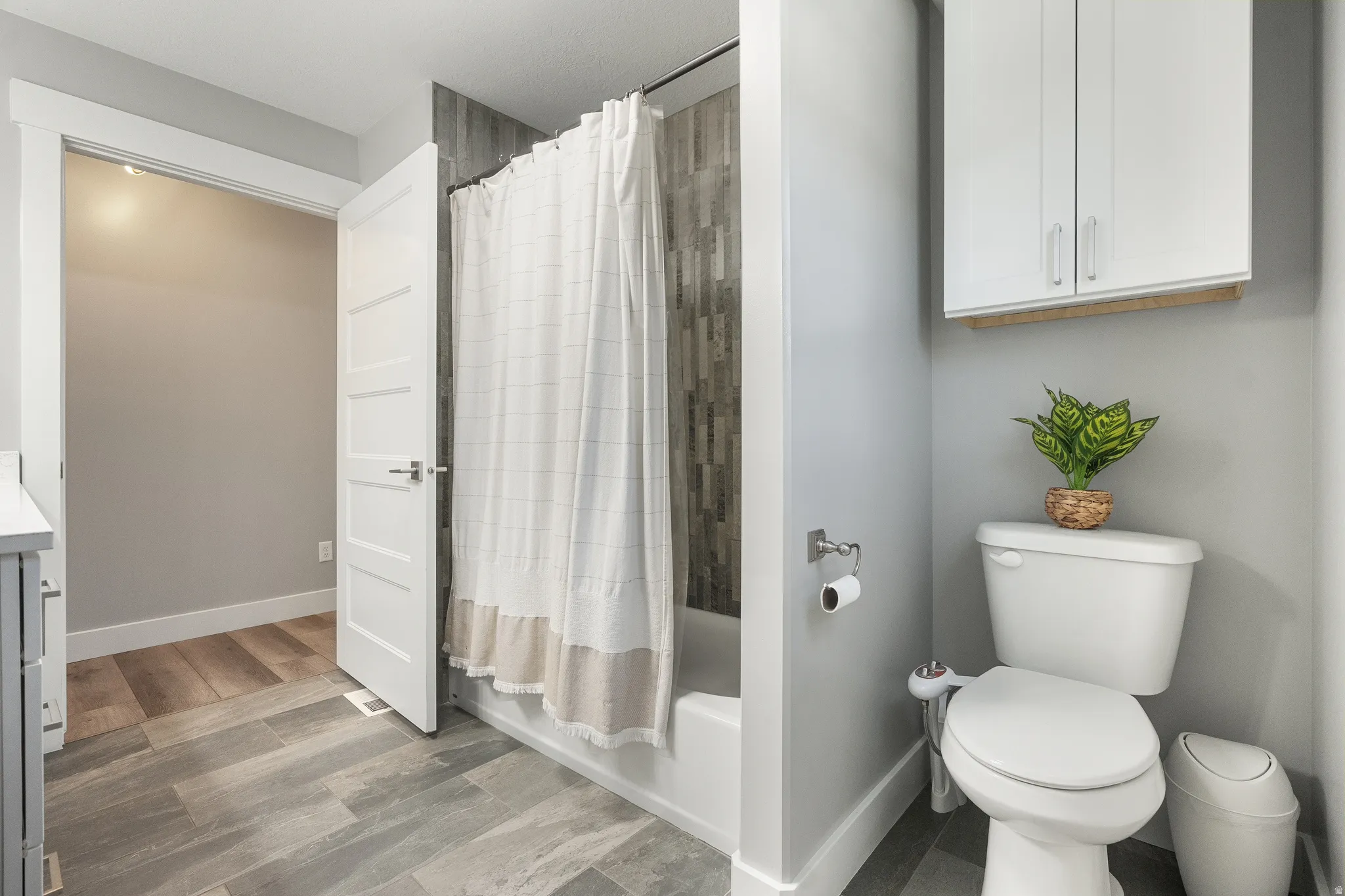 Full bathroom featuring a white tub/shower combination with a vertically tiled surround, white toilet, and wood-finish flooring