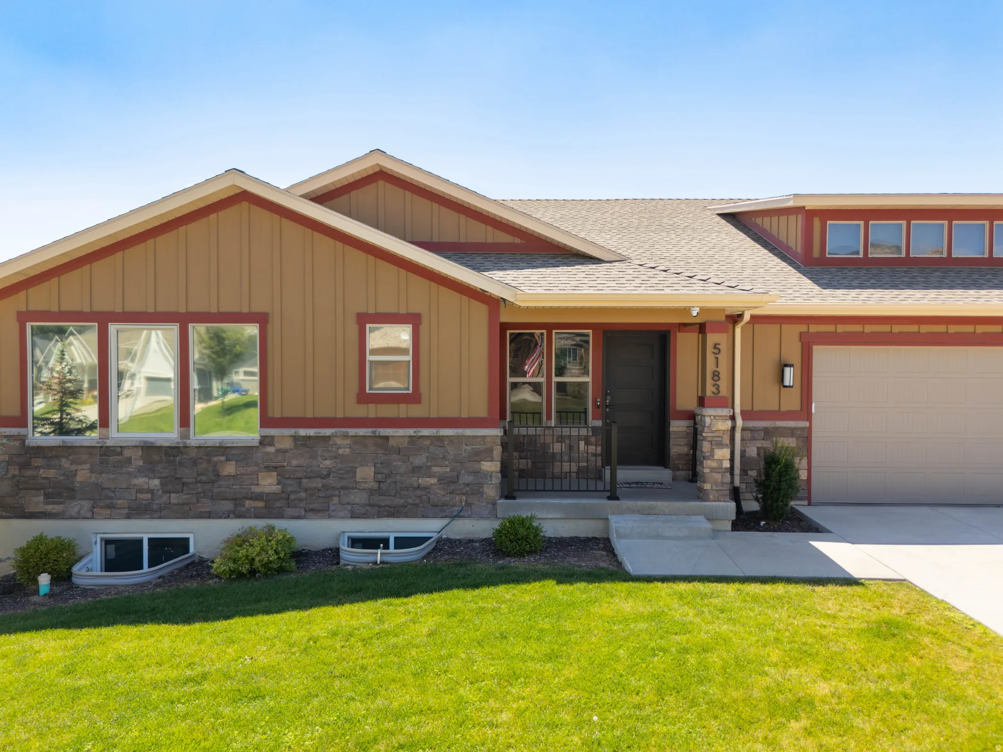 Contemporary exterior featuring stone veneer, vertical siding, a front entry with iron railing, an attached garage, and upper transom windows