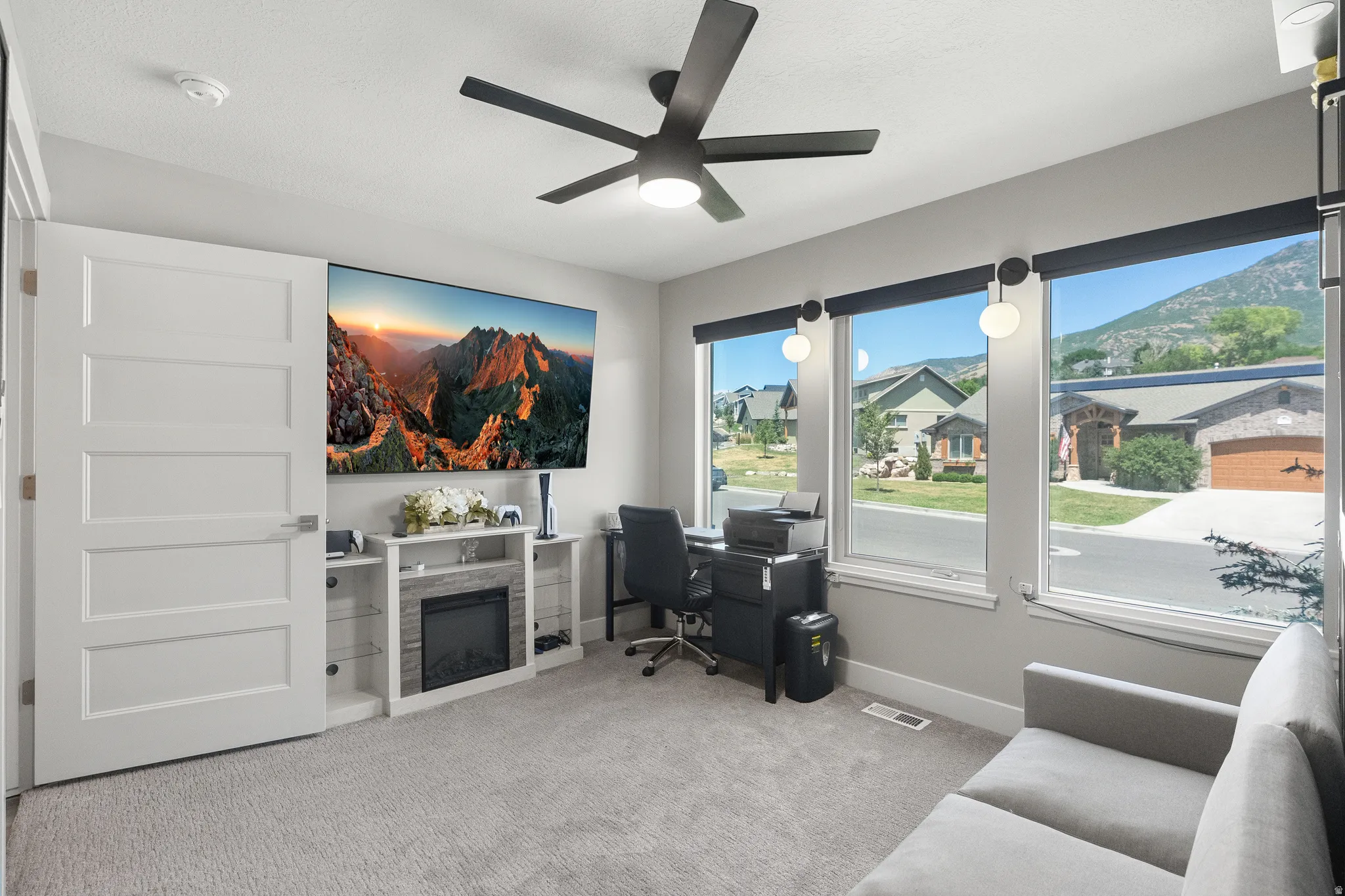 Bright room featuring large windows, a built-in electric fireplace with surrounding shelving, modern ceiling fan, and light gray carpet
