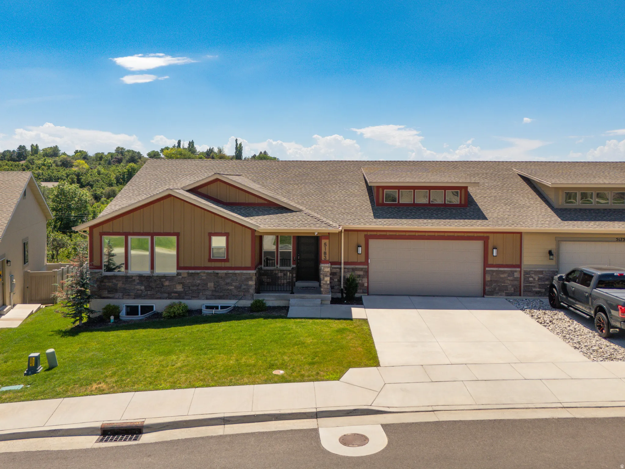 Split-level residence featuring a two-car garage, stone and siding exterior, front lawn, and concrete driveway