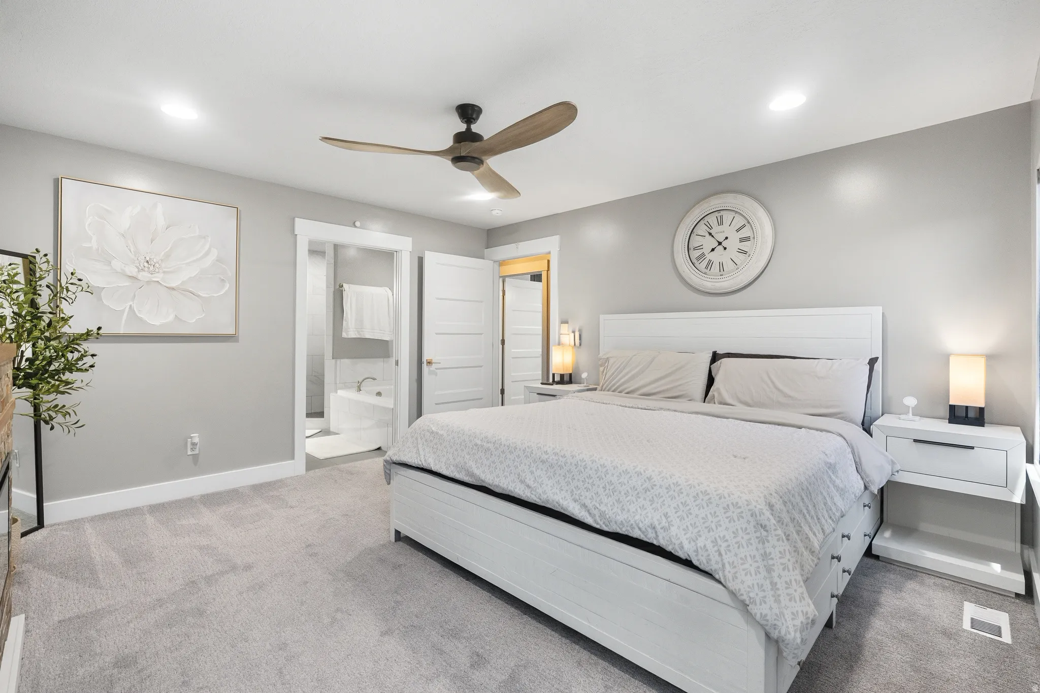 Carpeted bedroom with a ceiling fan, recessed lighting, and a white paneled door opening to a bathroom with a built-in tub