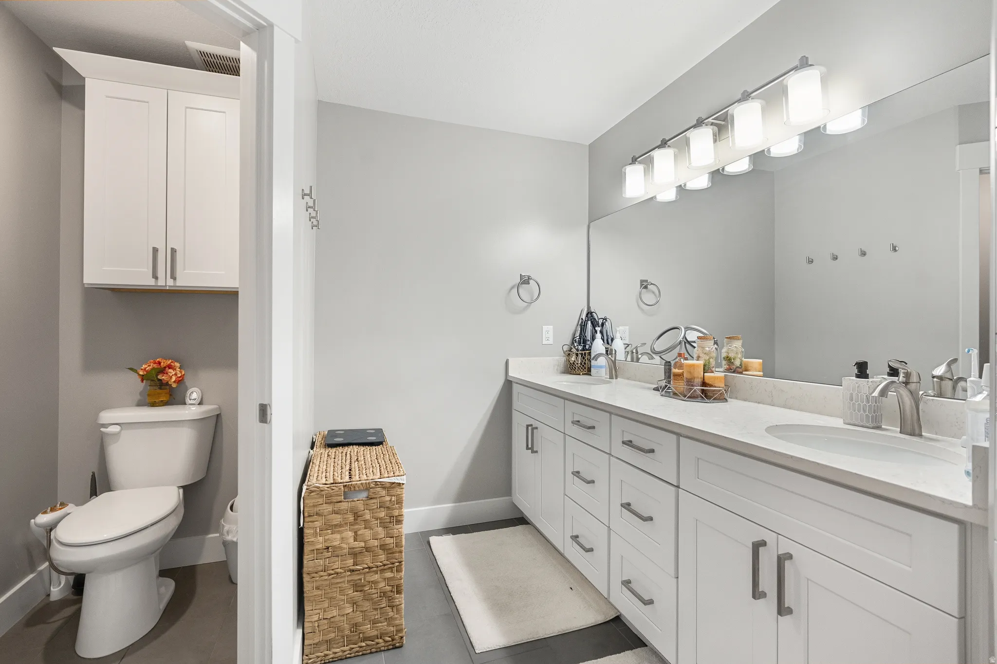 Bathroom featuring a dual vanity with white cabinetry and an integrated countertop, a large wall-mounted mirror, and a multi-bulb light fixture