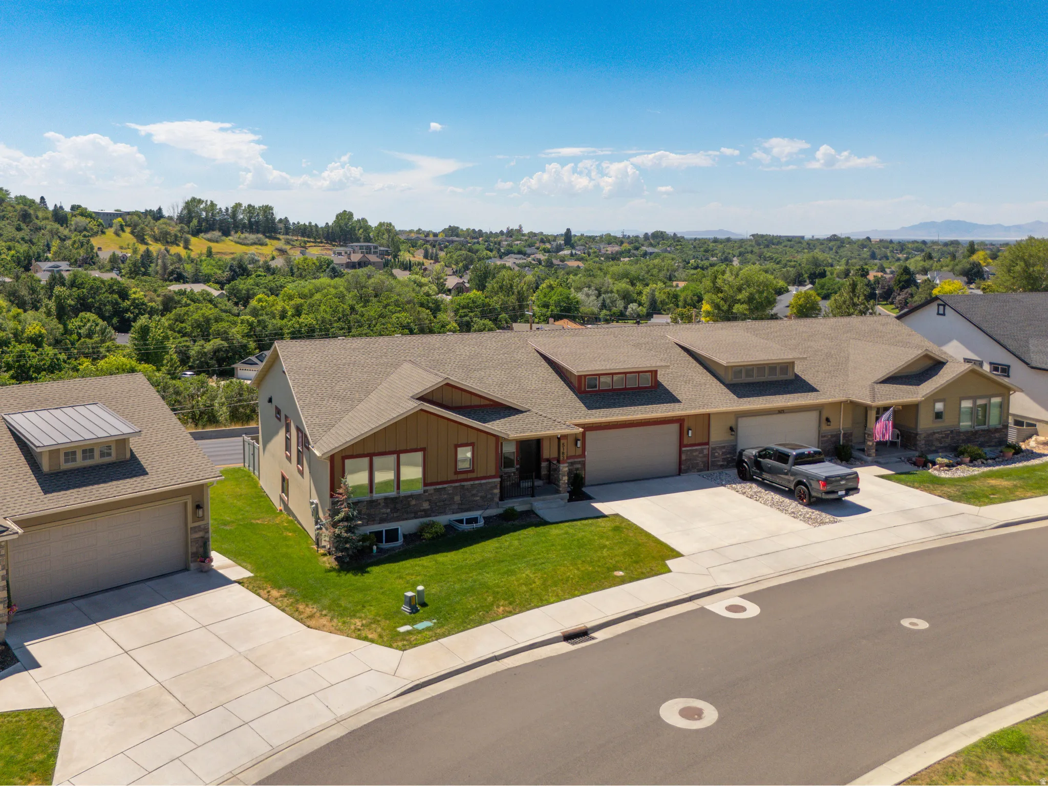 Contemporary-style residence featuring a stone and wood siding exterior, attached two-car garage, expansive concrete driveway, and a front yard with manicured lawn