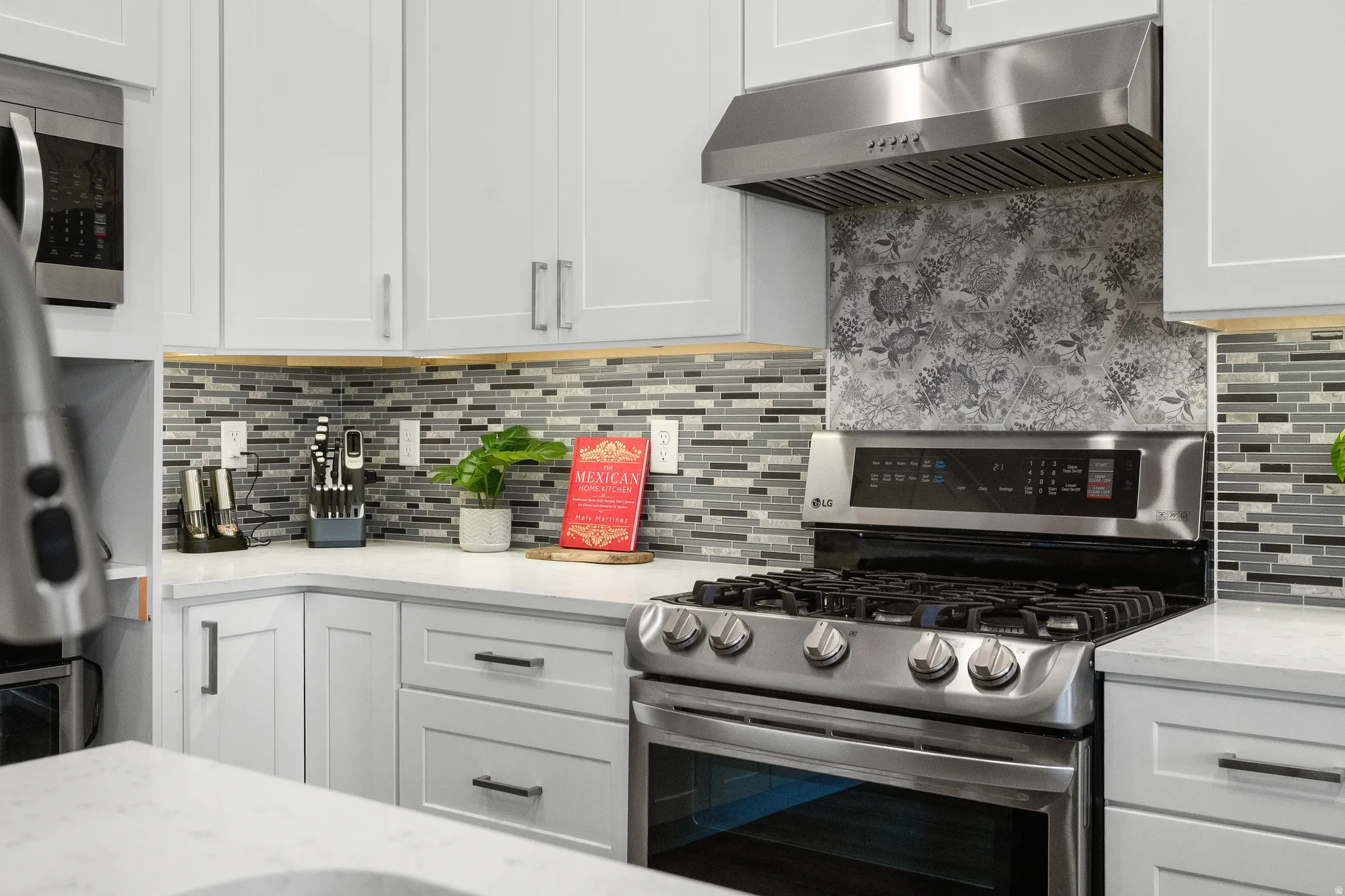 Contemporary kitchen featuring white cabinetry, quartz countertops, a mosaic tile backsplash, stainless steel gas range, and a coordinating stainless steel range hood