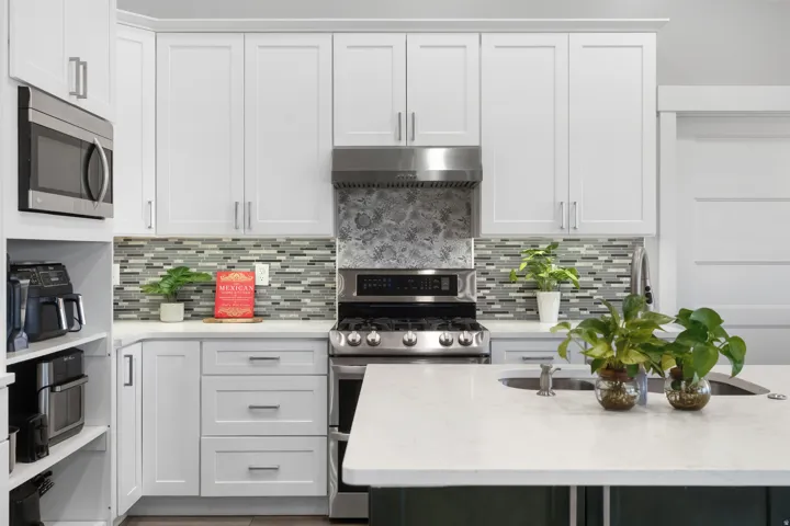 Modern kitchen featuring white shaker-style cabinetry, a built-in stainless steel microwave, a gas range with a matching range hood, and a mosaic tile backsplash