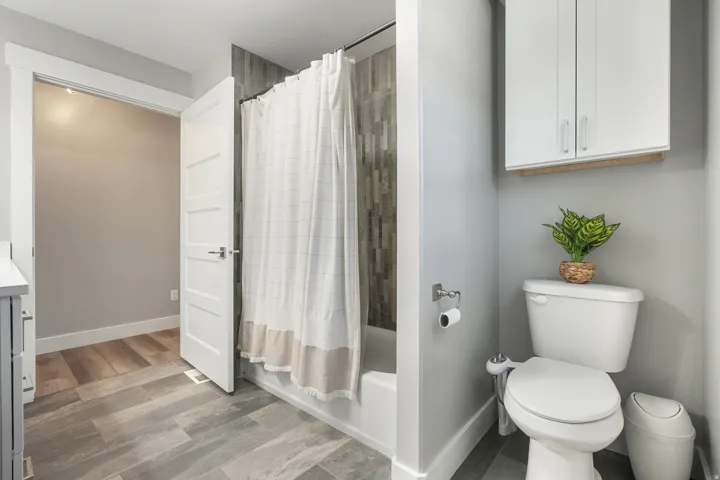 Full bathroom featuring a white tub/shower combination with a vertically tiled surround, white toilet, and wood-finish flooring