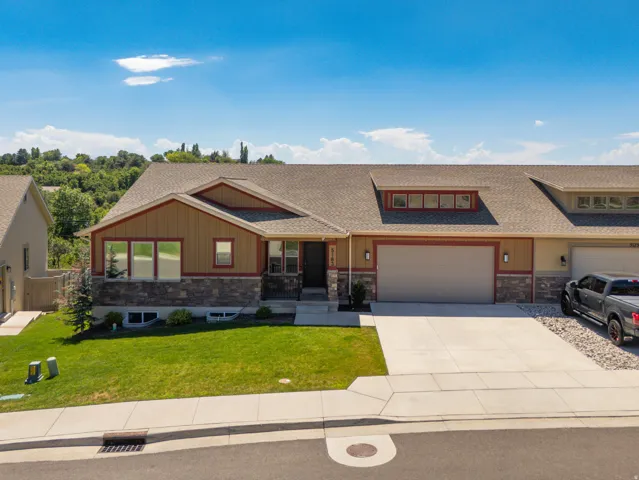 Split-level residence featuring a two-car garage, stone and siding exterior, front lawn, and concrete driveway