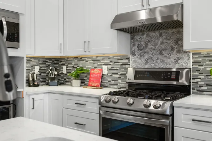 Contemporary kitchen featuring white cabinetry, quartz countertops, a mosaic tile backsplash, stainless steel gas range, and a coordinating stainless steel range hood