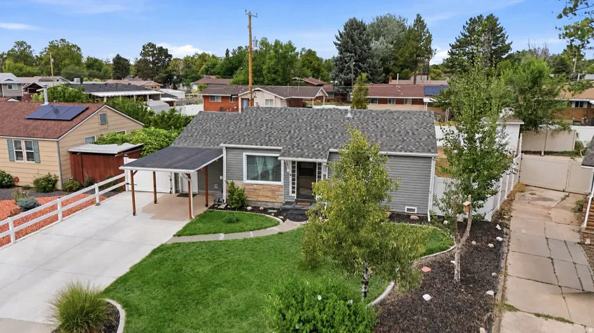 Gray siding exterior with stone accents, a dark shingle roof, a covered carport, a concrete driveway, and a landscaped front yard with a manicured lawn