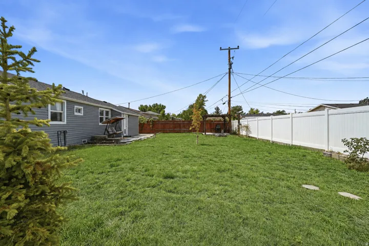 Expansive backyard featuring a manicured lawn, white privacy fencing, and a built-in stone patio
