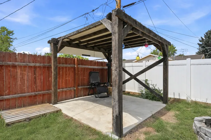 Outdoor pergola structure with a concrete pad, surrounded by a wood privacy fence and a white vinyl privacy fence