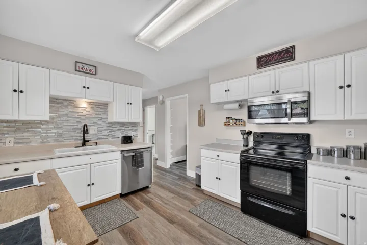Kitchen featuring white cabinetry, wood-finish flooring, light-toned countertops, a stainless steel dishwasher, and a black oven range with an above-range microwave