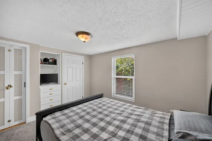 Bedroom featuring a built-in storage unit with drawers and shelving, a single window with horizontal blinds, textured ceiling, and neutral wall paint
