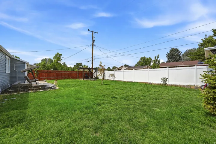 Expansive backyard featuring a lush lawn, a paved patio area, and a white privacy fence