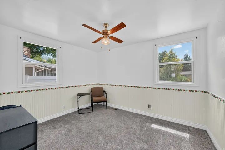 Room featuring two windows, a ceiling fan with integrated lighting, textured wall paneling, and wall-to-wall carpeting