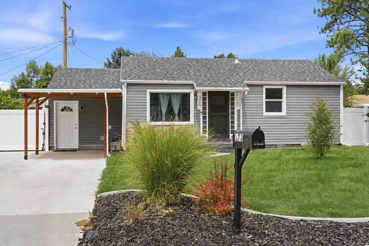 Gray siding exterior with a partial stone facade, a covered entry, an attached garage, and a manicured lawn