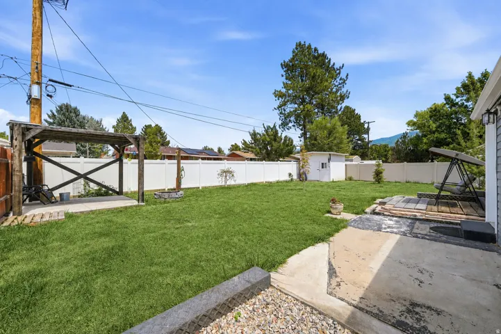 Expansive backyard featuring a lush lawn, white vinyl fencing, a concrete patio, a wood pergola, and a storage shed
