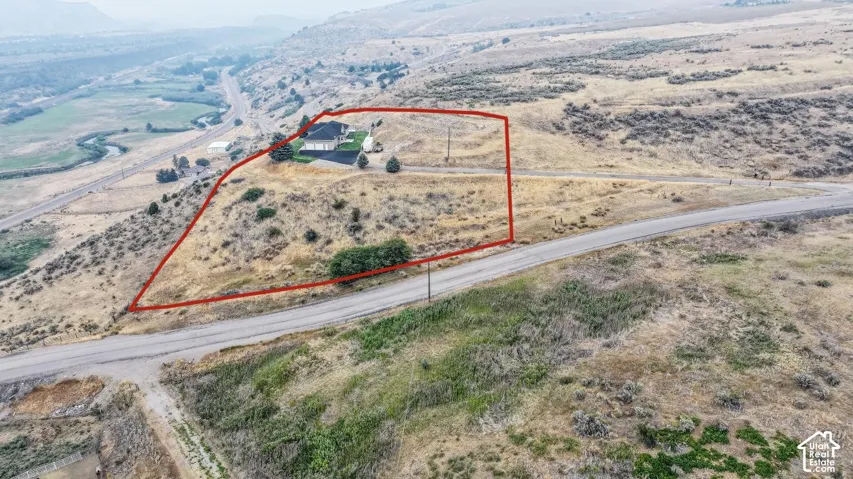 Expansive rural acreage with a single-family residence, featuring a paved driveway, mature landscaping, and a surrounding natural landscape