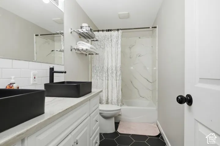Bathroom featuring a dual vanity with black vessel sinks and matte black faucets, white subway tile backsplash, white cabinetry, and a textured countertop