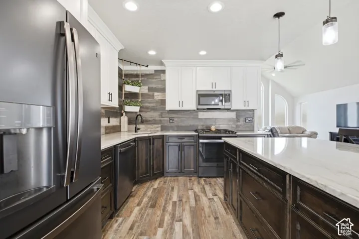 Gourmet kitchen with stainless steel appliances, two-tone cabinetry, wood-finish flooring, white countertops, and a wood plank backsplash