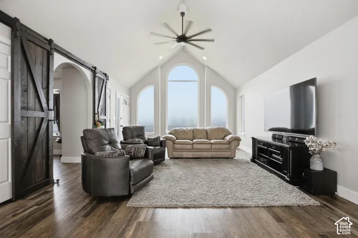 Vaulted ceiling living area featuring wood-finish flooring, a contemporary ceiling fan, and arched windows