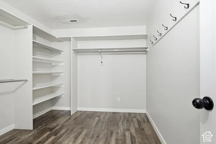 Walk-in closet featuring white built-in shelving, hanging rods, and wood-finish flooring