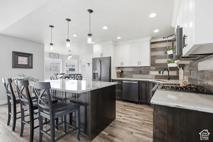 Spacious kitchen featuring a large island with seating, white shaker-style upper cabinetry, dark lower cabinetry, wood-finish flooring, and quartzite countertop