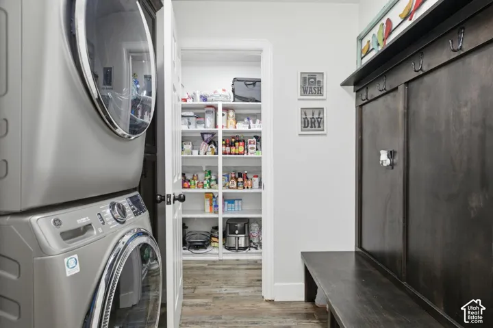 Dedicated laundry area featuring a stacked washer and dryer, wood-finish flooring, and a built-in pantry with white shelving