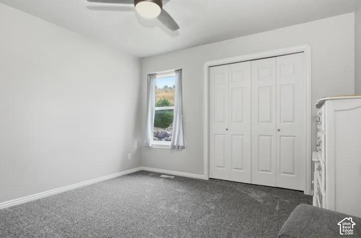 Bedroom featuring neutral gray walls, gray carpet, a ceiling fan with integrated lighting, a window with distant landscape, and a closet with bi-fold doors