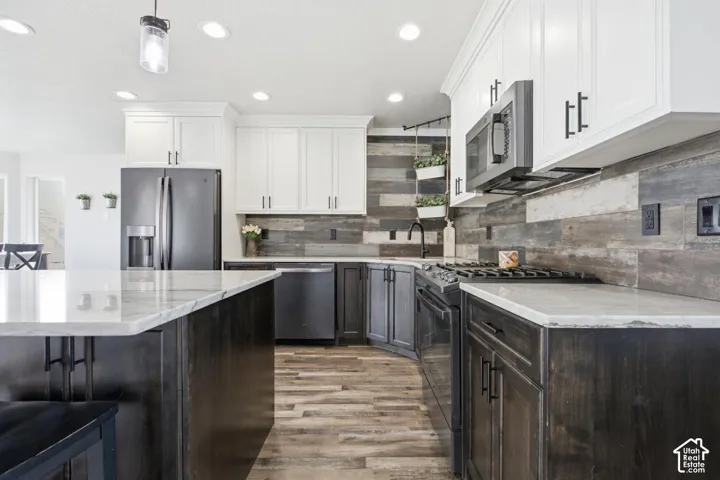 Modern kitchen featuring a large island with a light-toned countertop, contrasting dark wood-finish cabinetry, stainless steel appliances, a wood plank accent wall, and recessed lighting