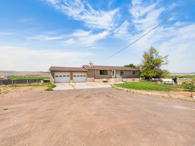 Ranch-style residence featuring a two-car garage, front entry with white railing, and a broad unpaved driveway
